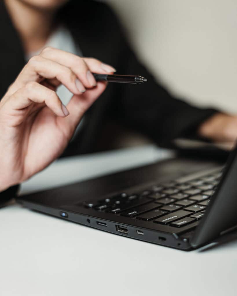 Foto di una persona in abbigliamento formale che tiene una penna sopra una tastiera di laptop, simbolo di analisi o pianificazione professionale