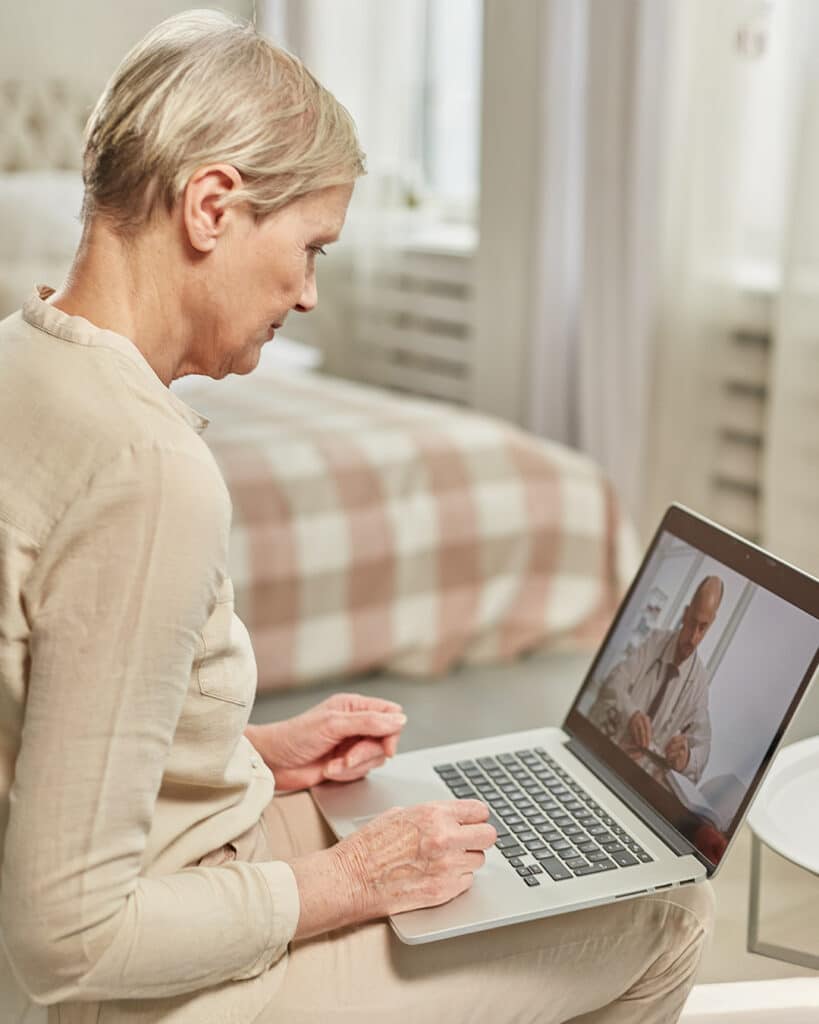 Foto di una signora di età senile, seduta dietro al pc, che guarda un video a tema sanitario